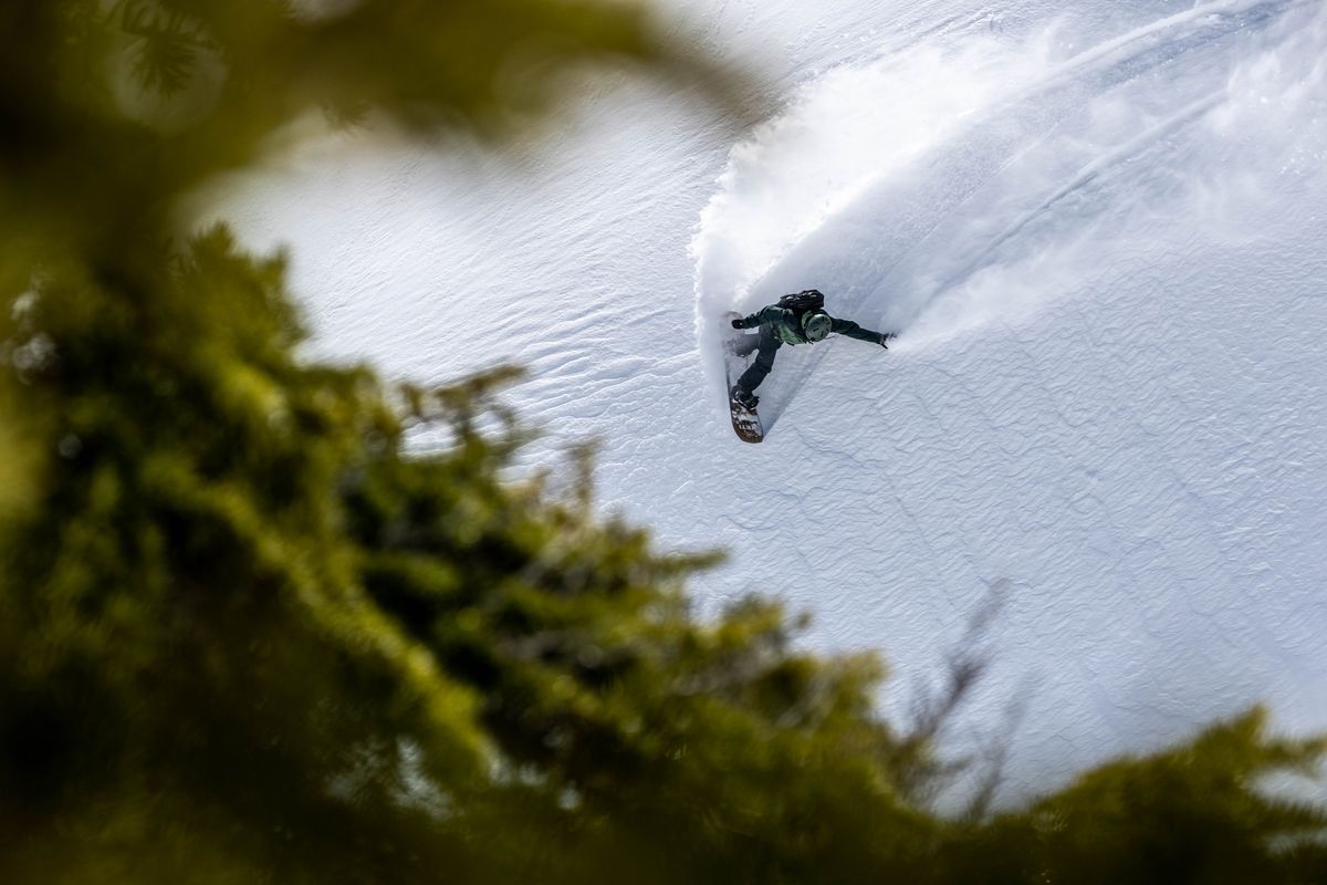 Snowboarder slashing powder framed by trees at Mt Baker