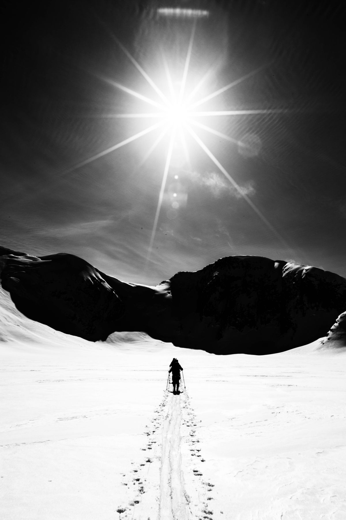 Lone ski tourer under a sunstar on a backcountry skin track